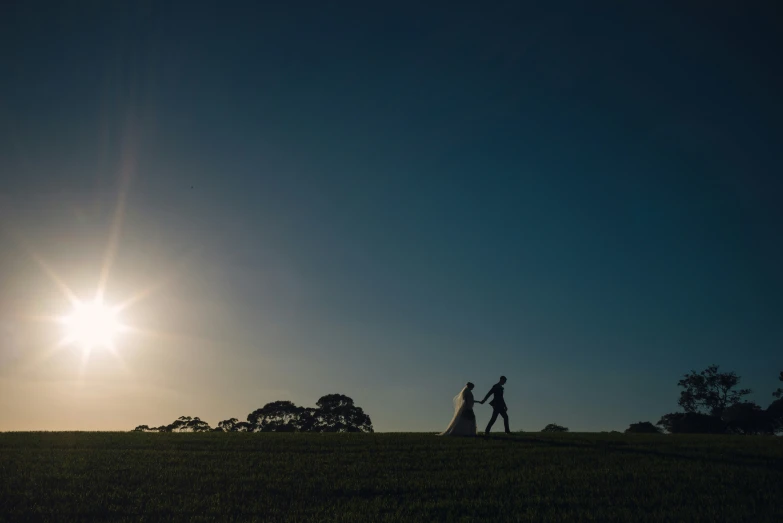 the couple are walking in the field at sunset