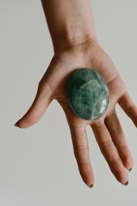 a person's hand holding a green crystal ball