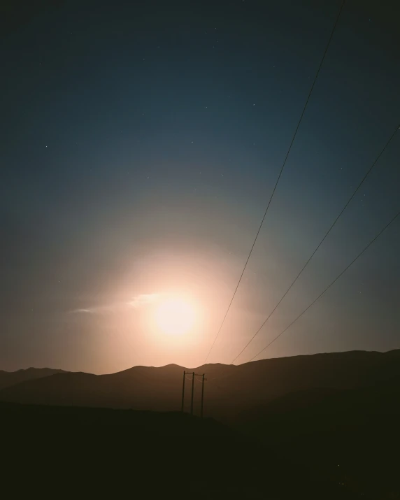 a field with power lines in the sky with the sun behind them