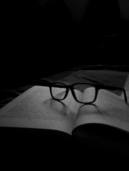 a black and white image of glasses resting on an open book