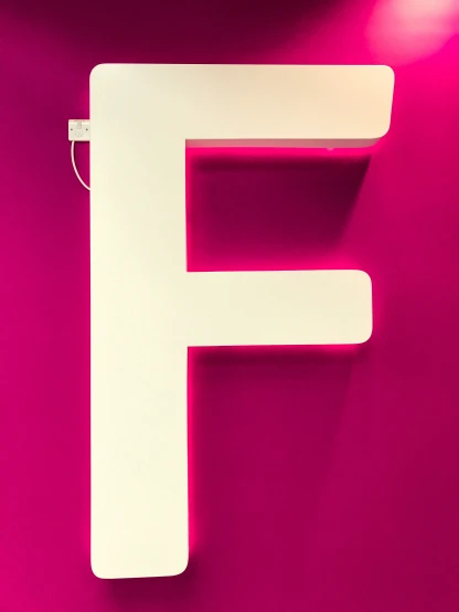 a neon pink and white f wall mounted to a purple background