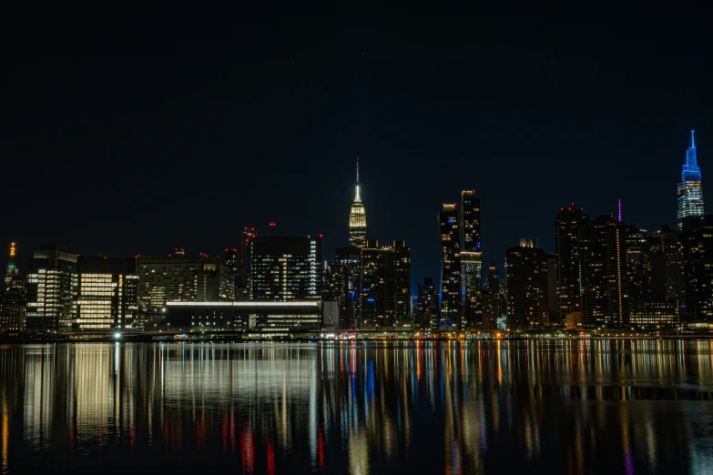 a night time view of the city skyline with a river reflecting off it