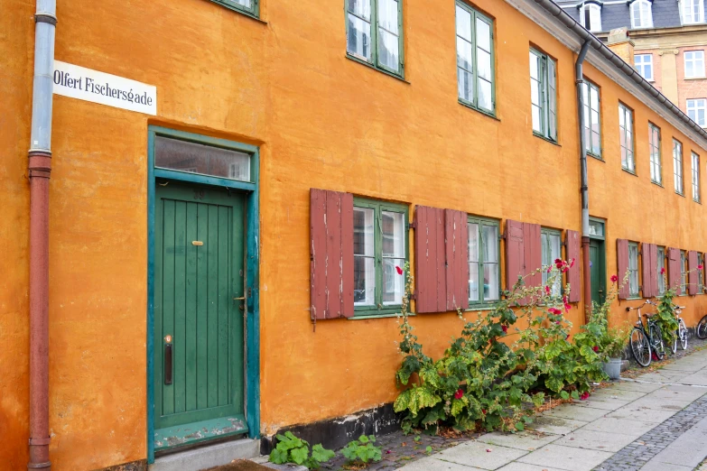 a long, orange building with red shutters with two bikes parked outside