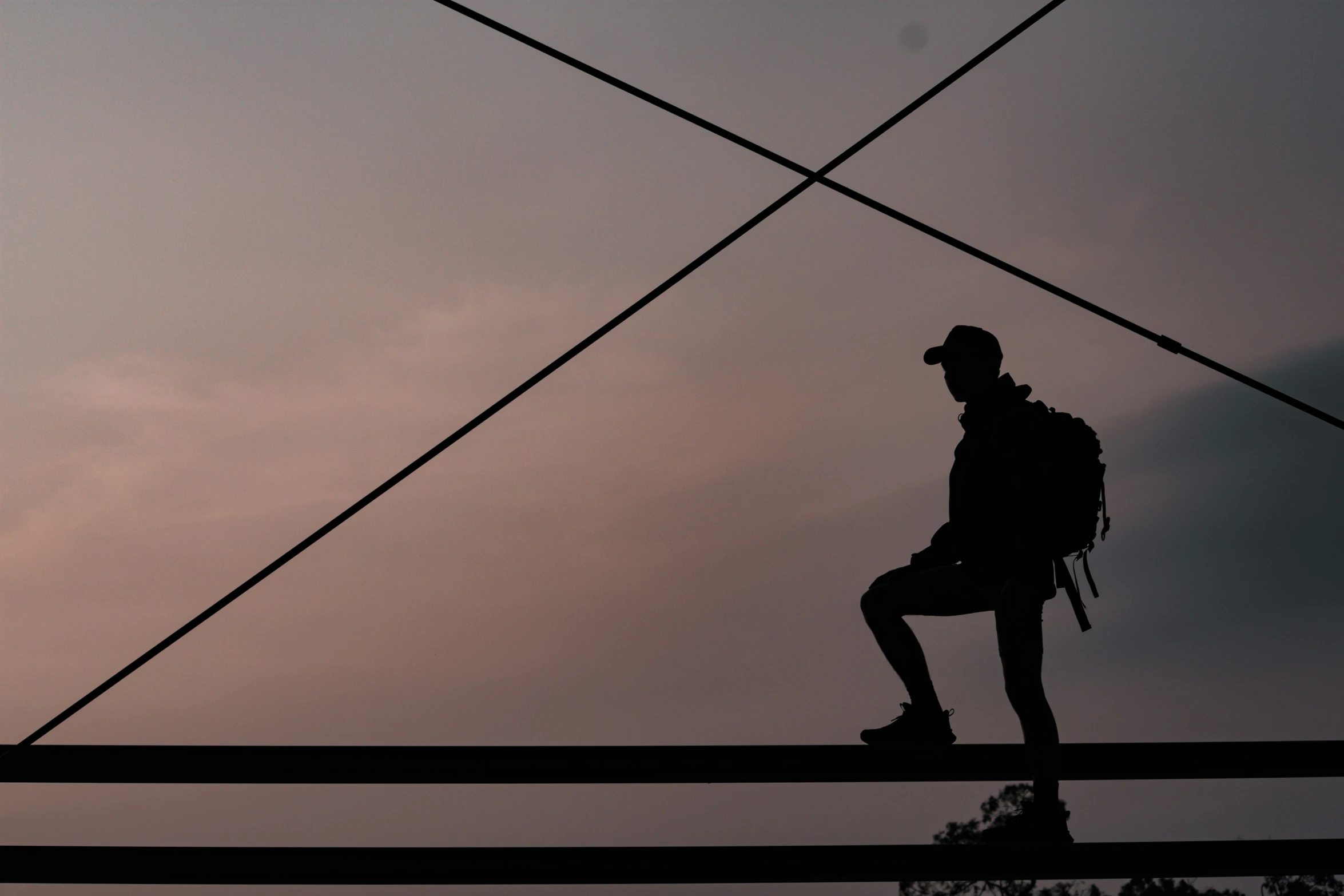 a man in a hat sitting on a pole as the sun is setting