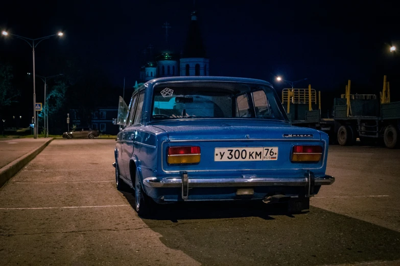 an old blue car is on the street with a building in the background