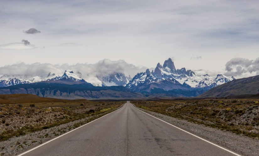 a road with mountains and snow capped peaks in the background