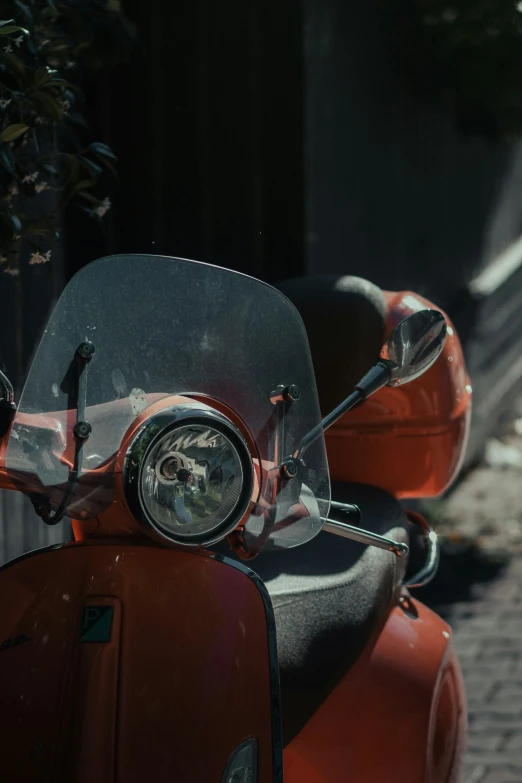 an orange scooter parked on a sidewalk next to a tree