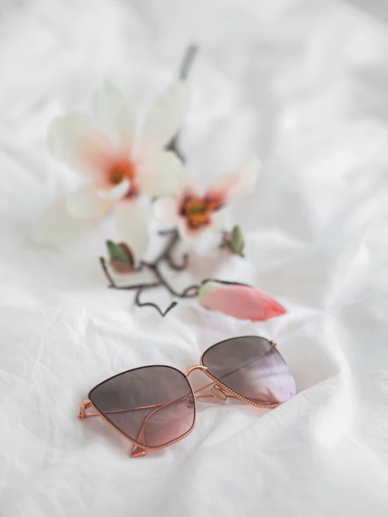 a pair of sunglasses on a bed with flowers in the background