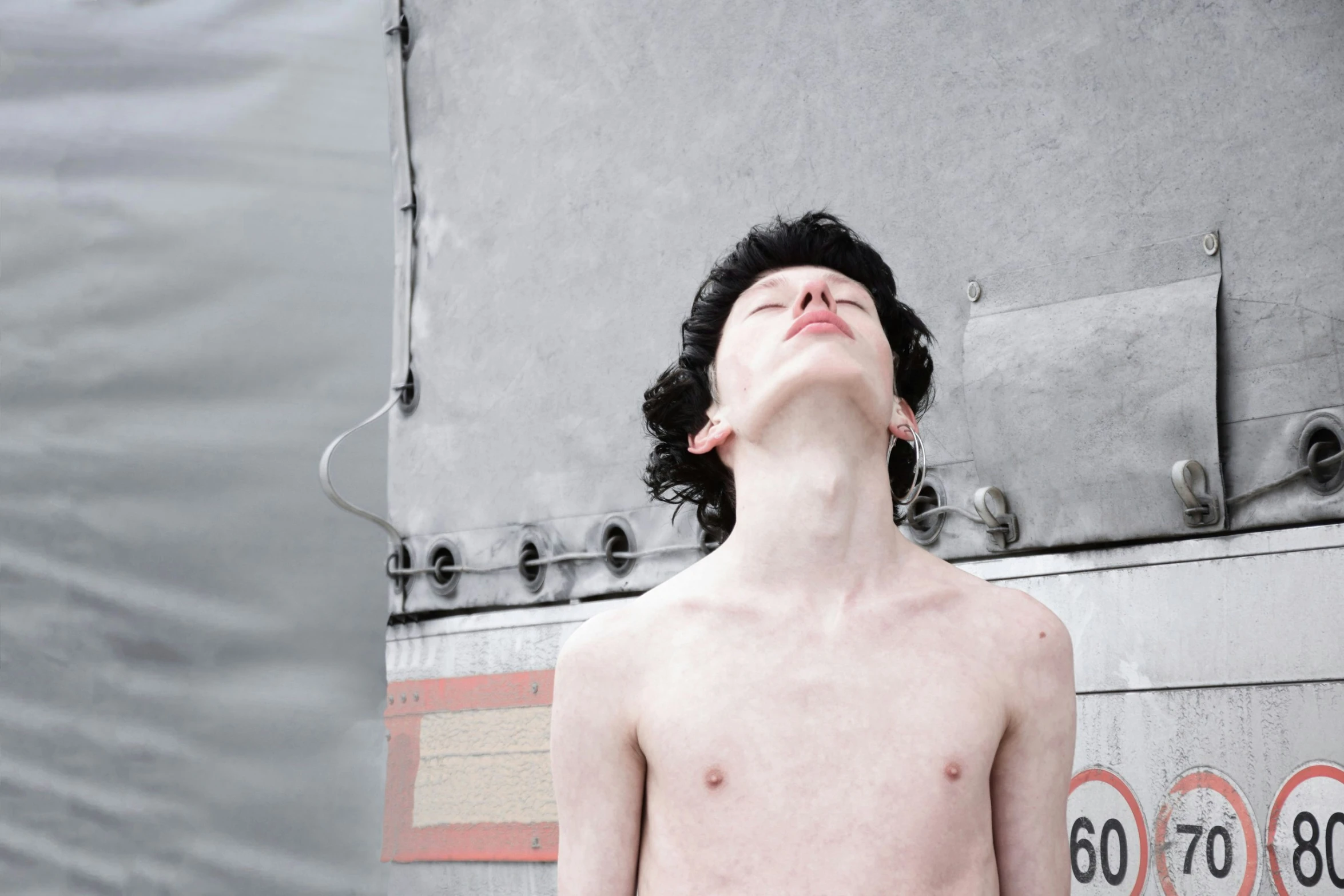 a young man with black hair standing against a wall looking up