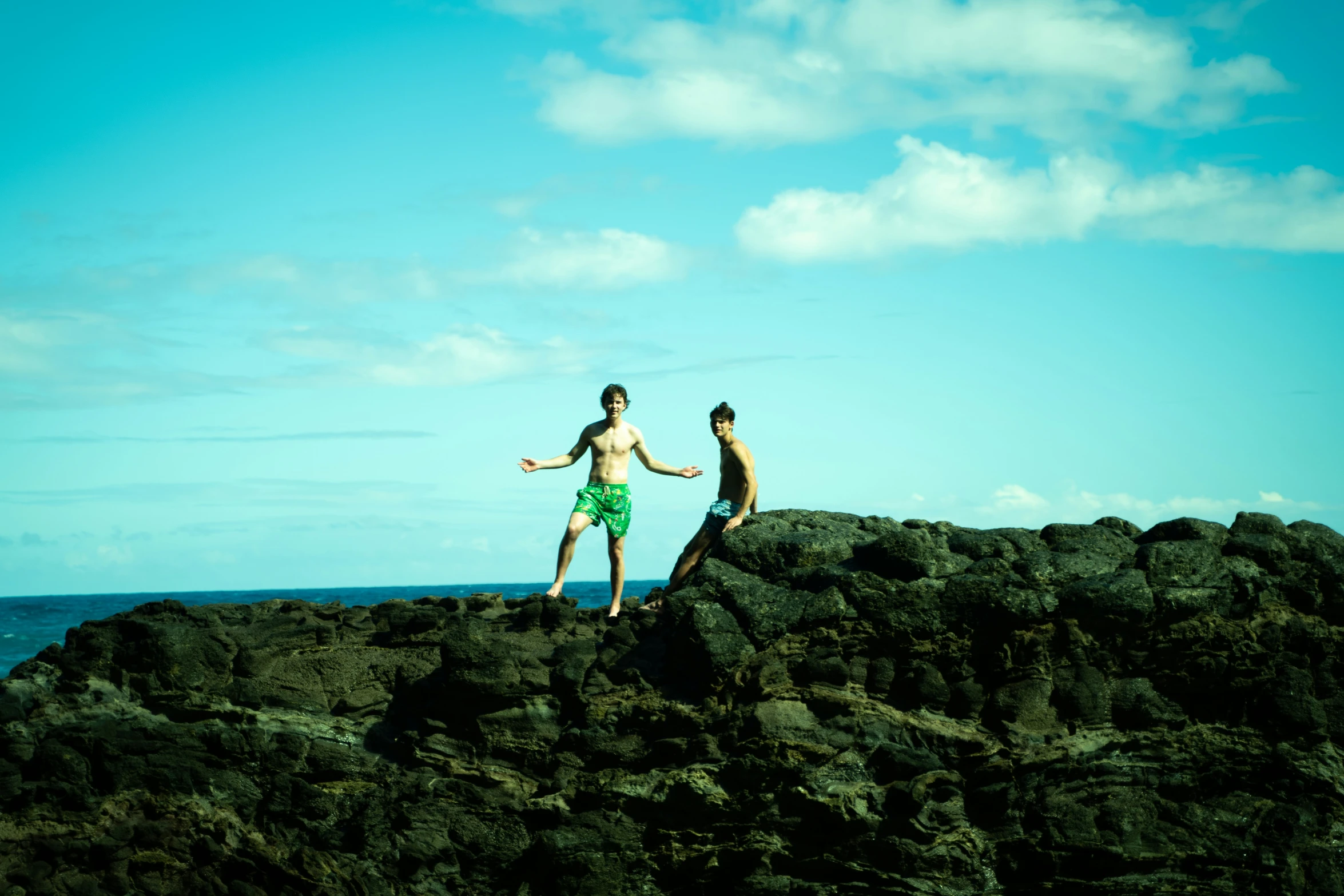 two men running along a rocky shore under a blue sky