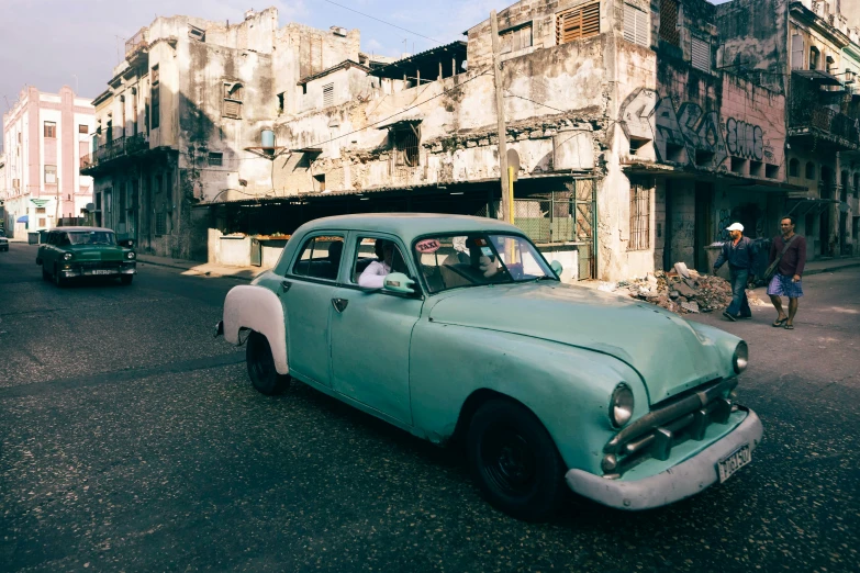 a green car driving down a street near buildings