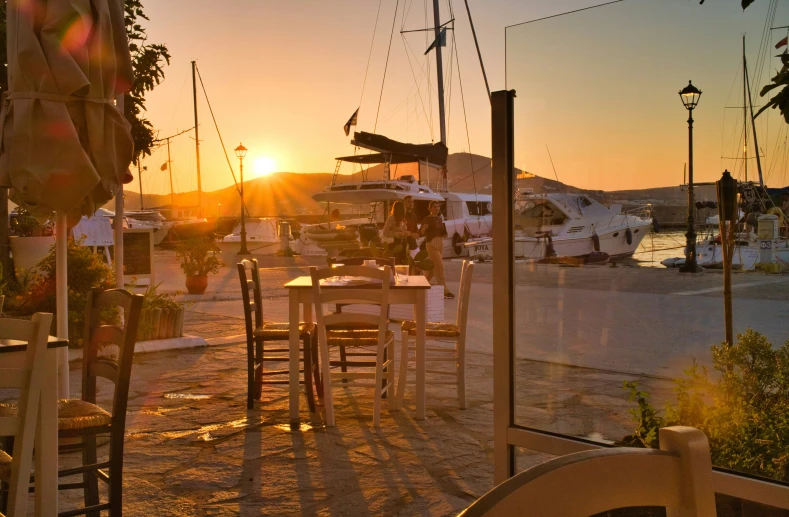 the sun sets over a marina with tables and chairs