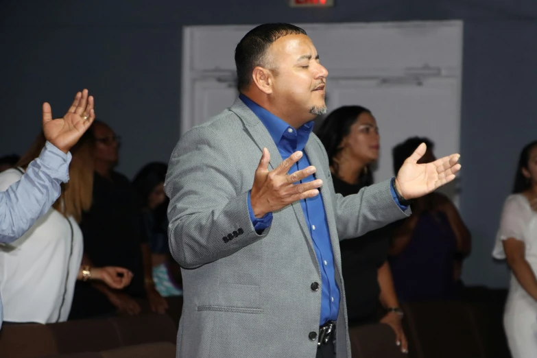 a man in a suit stands next to other people, clapping