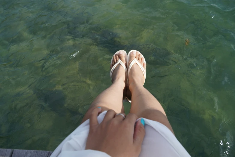 a person wearing sandals standing at the water's edge with her feet up in the water