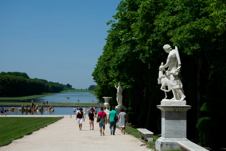 people walking down the path in front of a pond