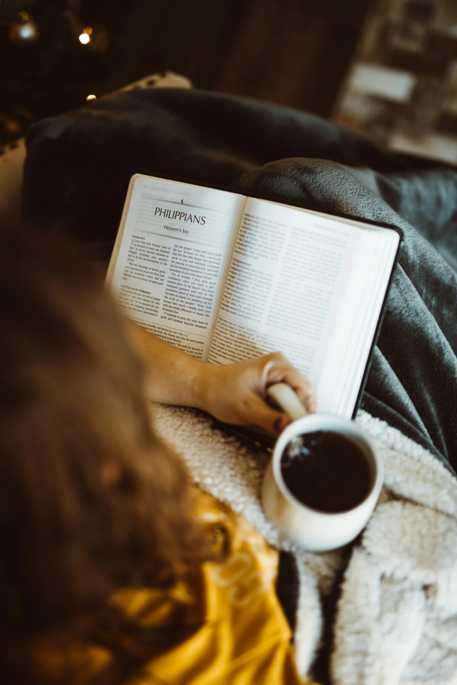 the open book is next to a cup of coffee on the bed