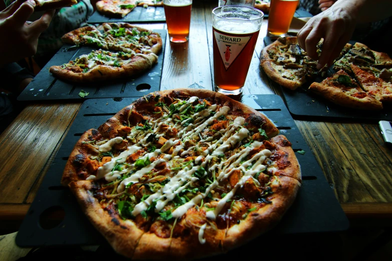 the table is covered in pizzas, beers, and glasses