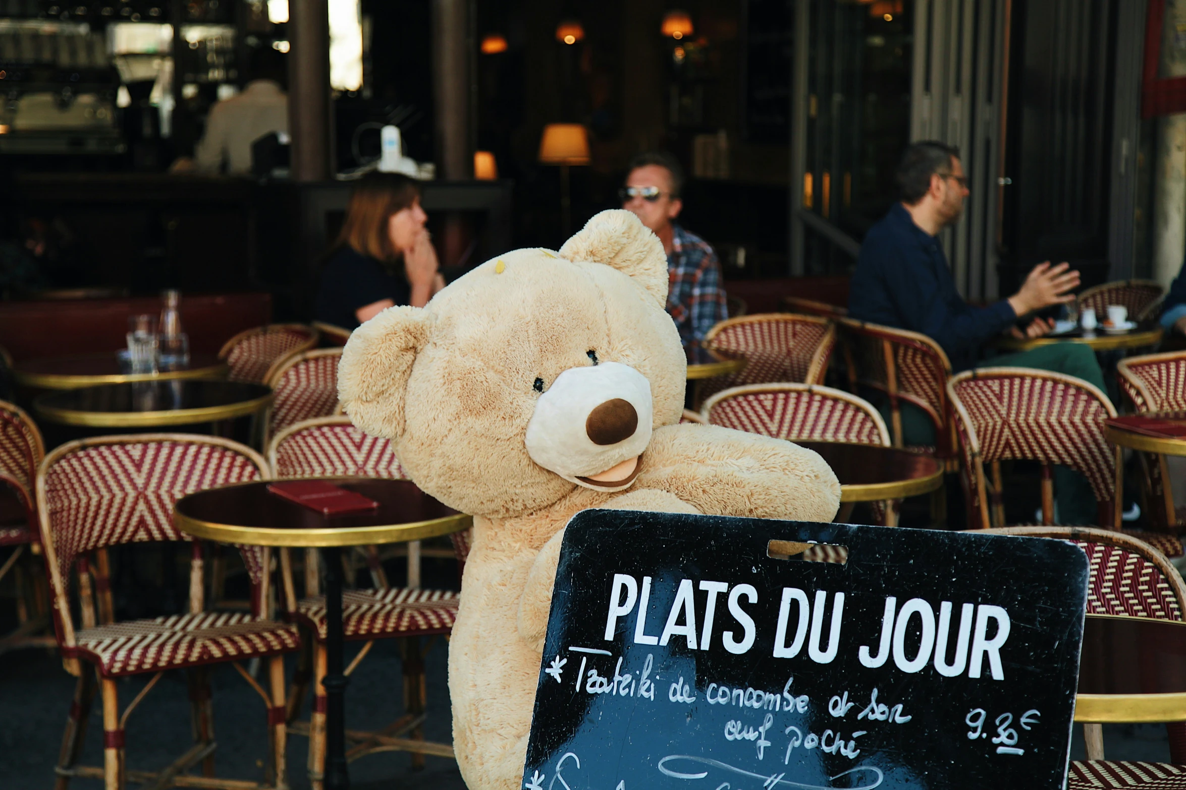 a large brown teddy bear holding onto a chalkboard