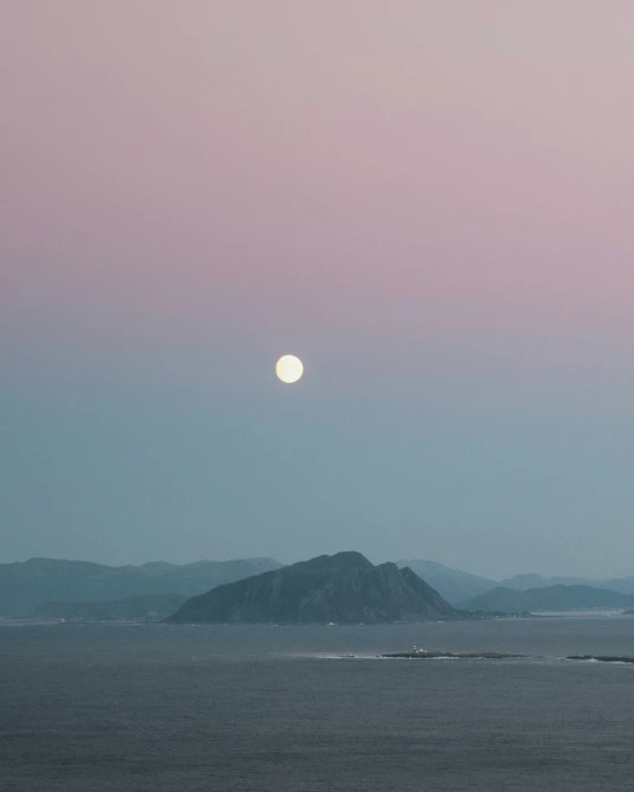 the moon setting over a distant island in the ocean