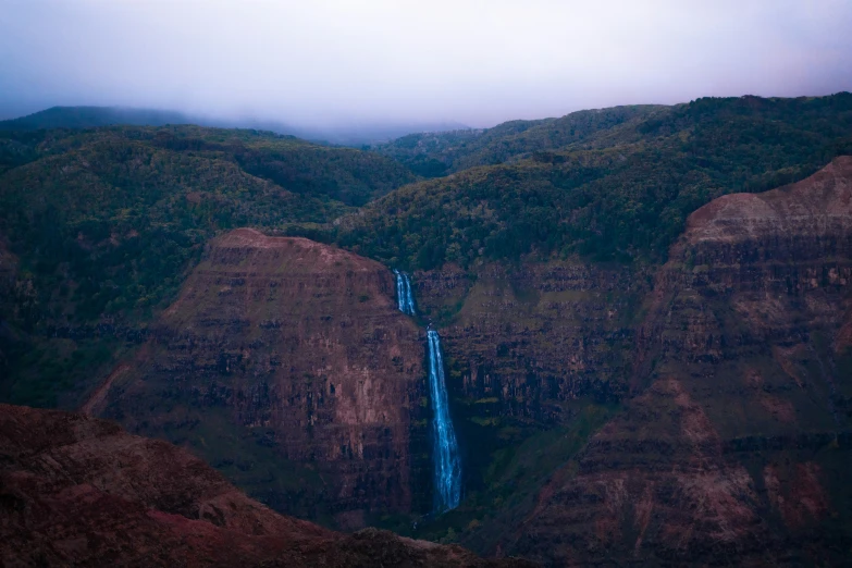 a large waterfall flows through the mountains in a foggy day