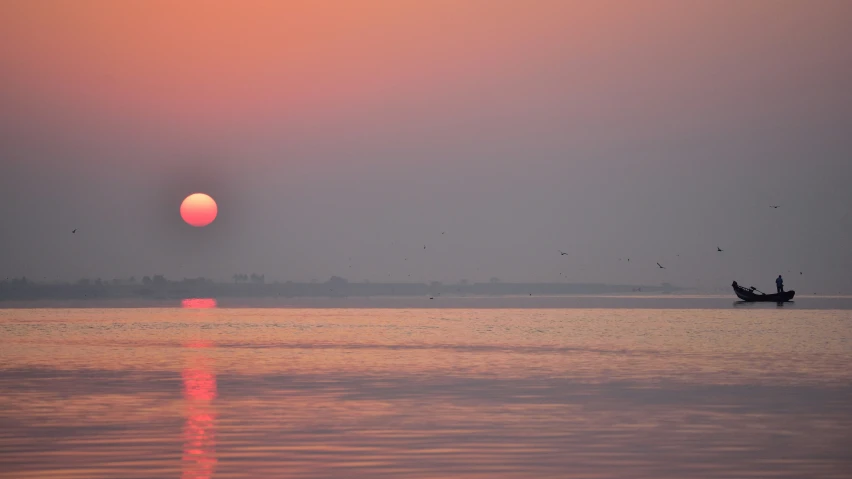 the sun is setting on the water with boat out to sea