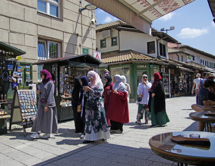 several women stand near shops selling merchandise