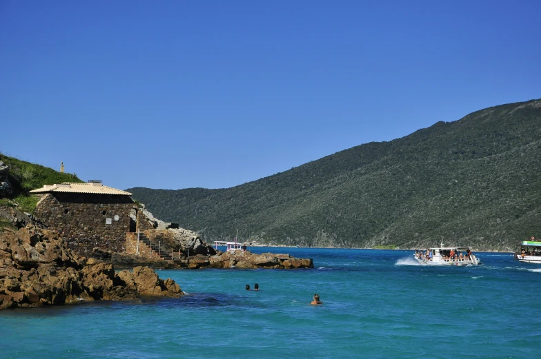 boats floating in a blue ocean next to a rocky shoreline