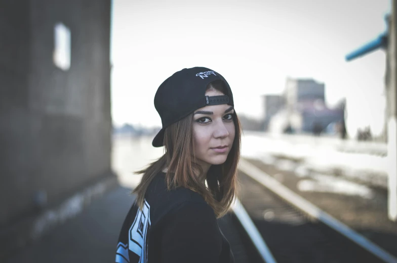 a girl poses for a pograph on the side of train tracks