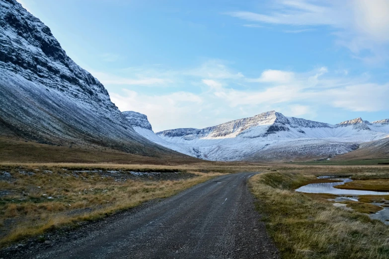 an empty dirt road surrounded by mountains under blue skies