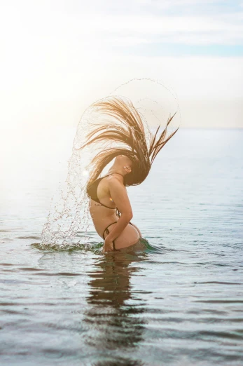 a woman standing in the water holding her hair back