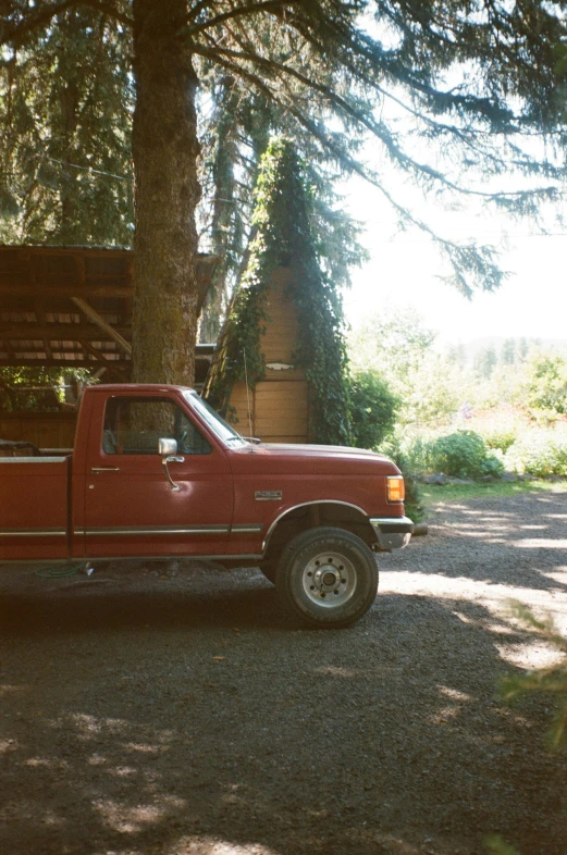 a red truck sitting next to a tree on the road