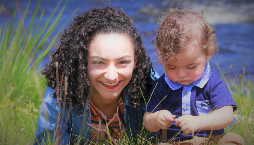 a woman laying in the grass holding a baby