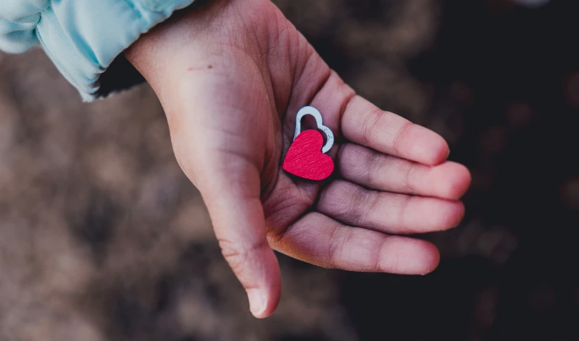 a hand holds an image of a red heart and key chain on it