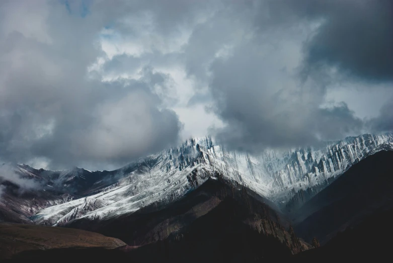 a mountain range covered in snow under a cloudy sky