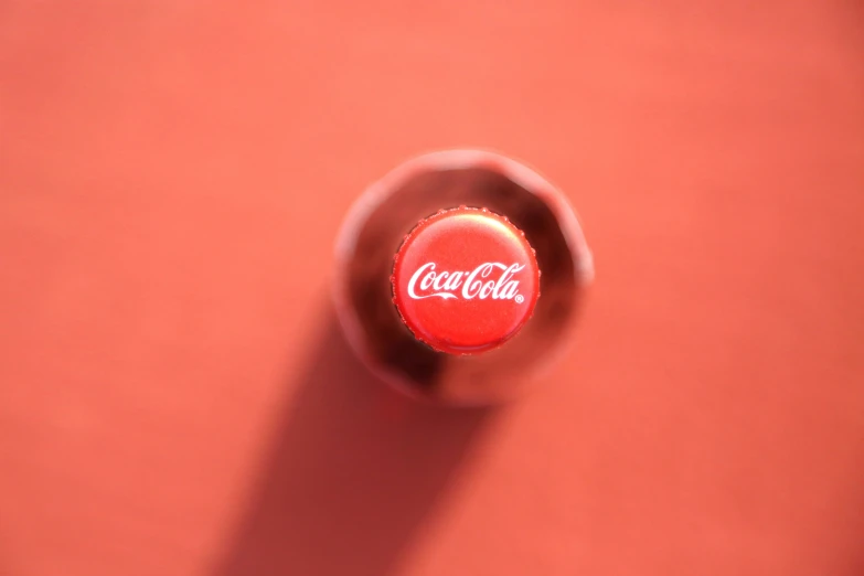 a single coke bottle sitting on top of a red surface