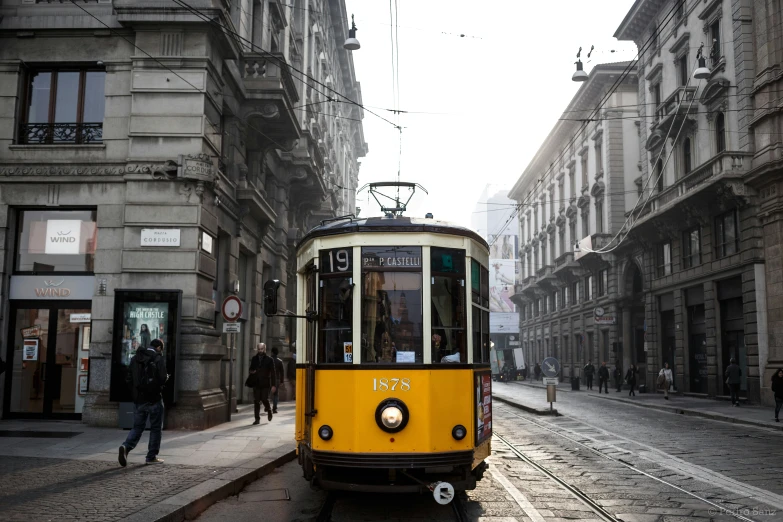 yellow and white train on tracks in a narrow city street