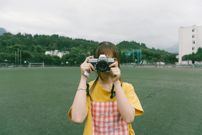 a woman in an orange and white plaid shirt taking a picture of her cell phone with the camera