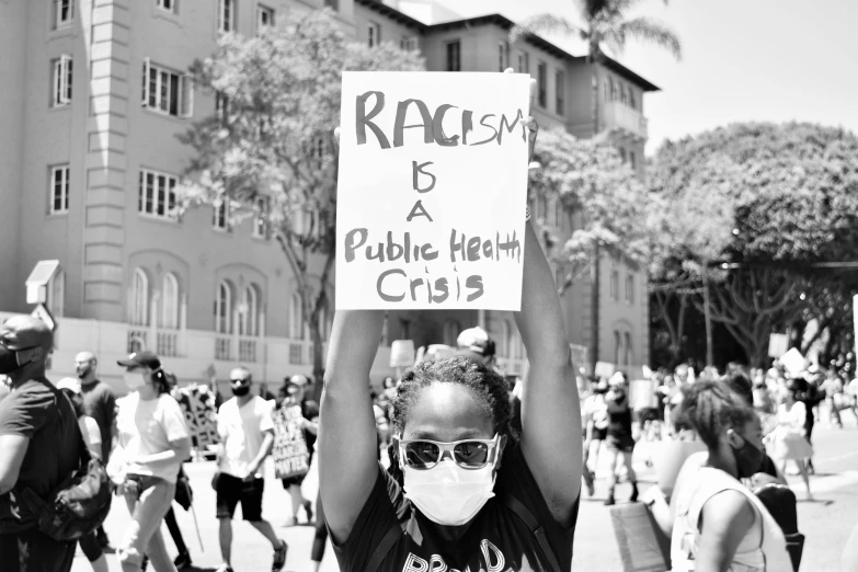 a person with glasses and a mask holds up a sign