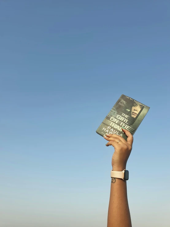 person holding up book in front of blue sky