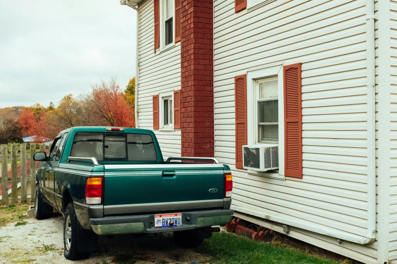 a green pick up truck is parked by a white building