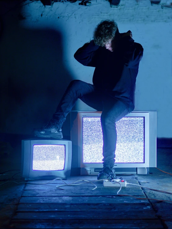 a man standing on top of two tvs while sitting on a stool