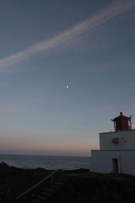 a lighthouse is silhouetted against the evening sky by the ocean