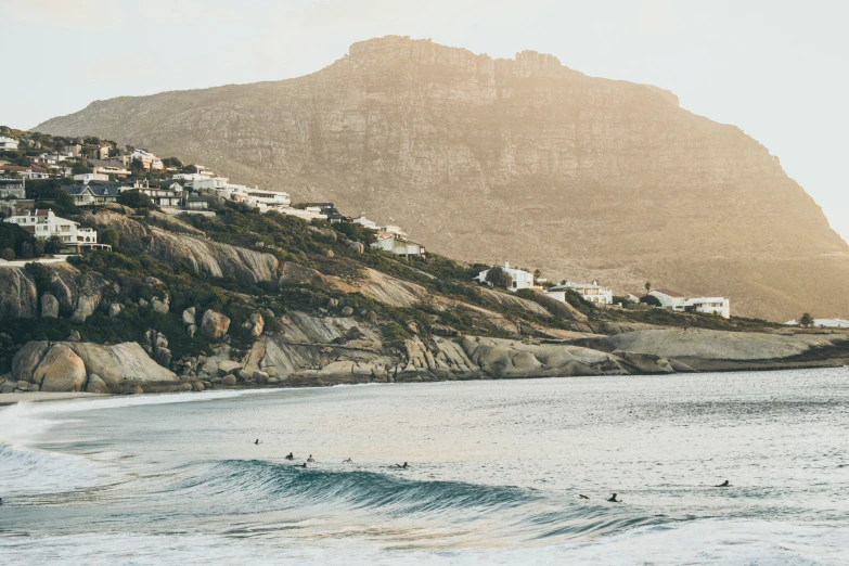 people riding the waves on the ocean under a mountain