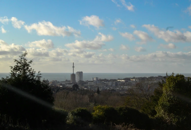 view of city, buildings and ocean with bright clouds in blue sky