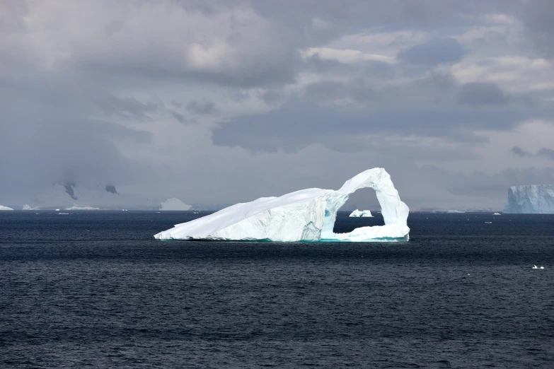 an iceberg floating in the ocean on cloudy day
