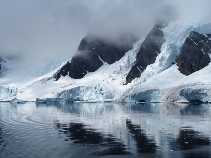 several snow covered mountains reflecting in a still river