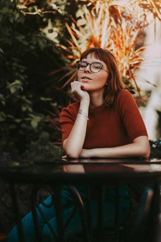 a young woman wearing glasses sits on a table next to some flowers