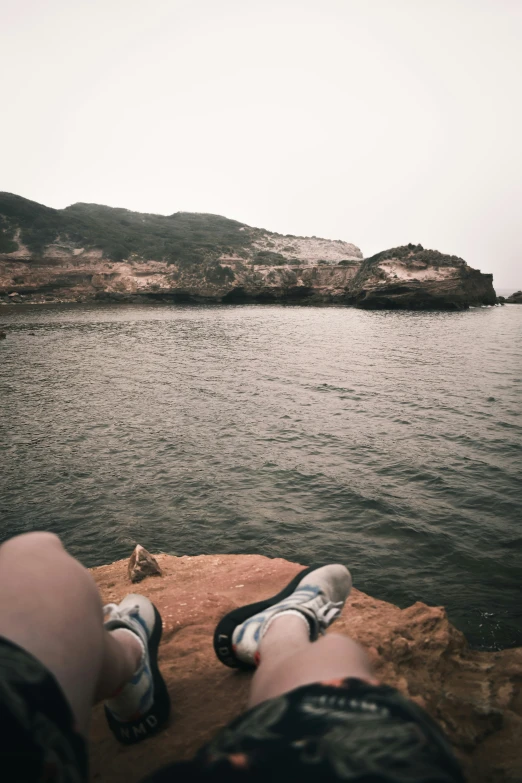 the legs of a person who is standing on a cliff by water