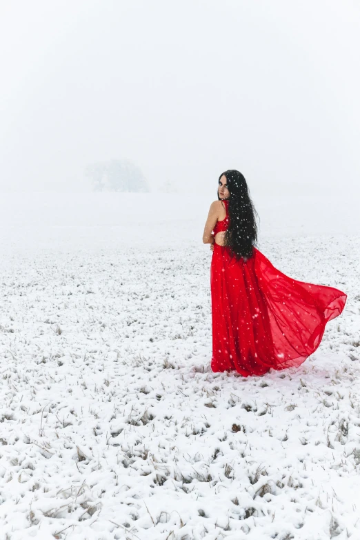 a woman in red dress with her arms over her shoulders walking through a snowy field