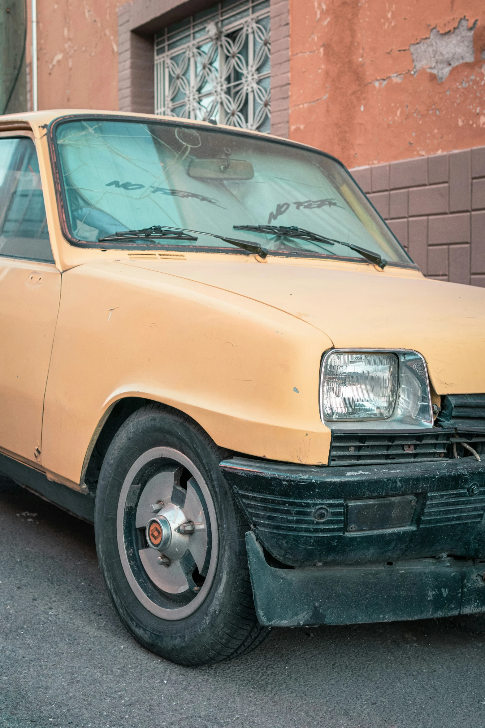 a dirty small yellow car parked in front of a building